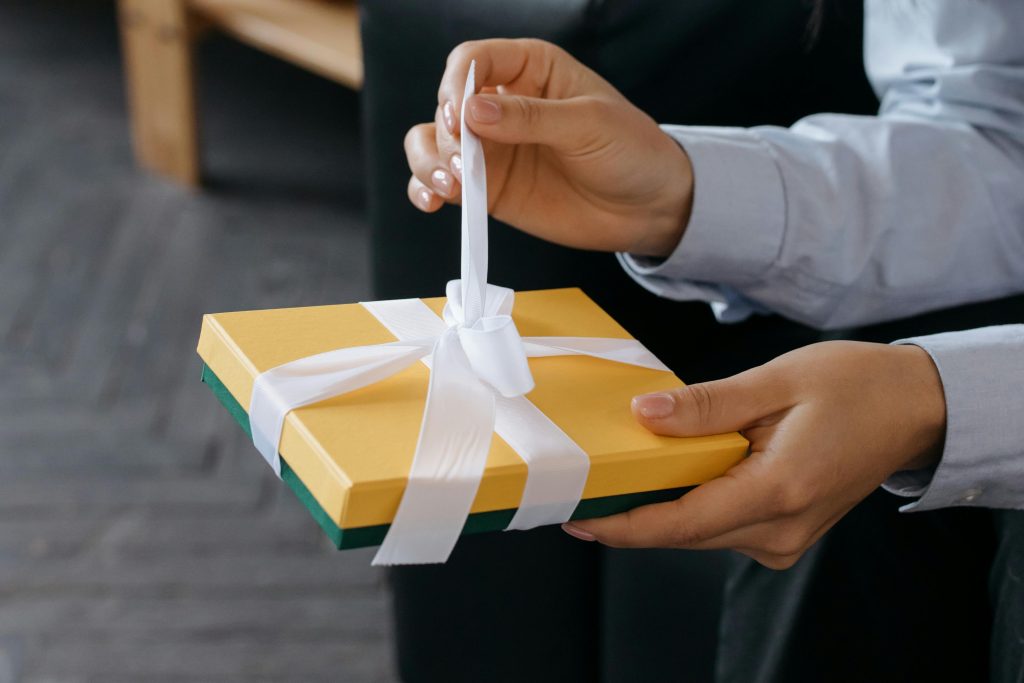 pexels photo 6650015 6650015 Close-up of hands untying a yellow gift box with a white ribbon indoors.